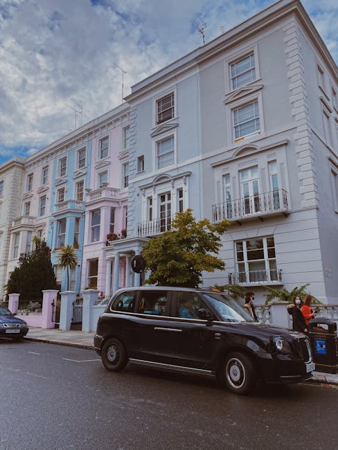 The image shows a row of multi-storey terraced houses with ornate white facades, bay windows, and small balconies, situated along a residential street. In the foreground, a black London-style taxi cab